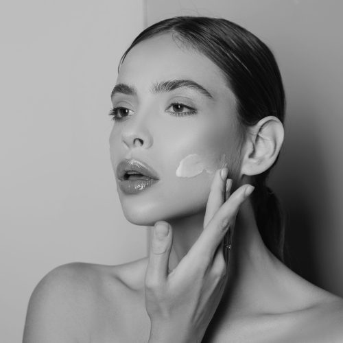 Attractive girl putting anti-aging cream on her face. Closeup Portrait Of Girl With Healthy Smooth Skin